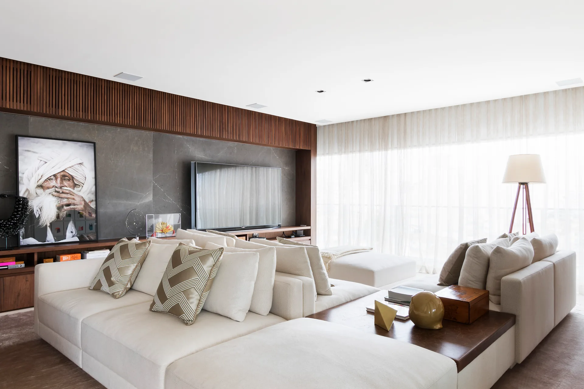 Living do Apartamento Alto de Pinheiros com sofá claro, painel de madeira e obra de arte