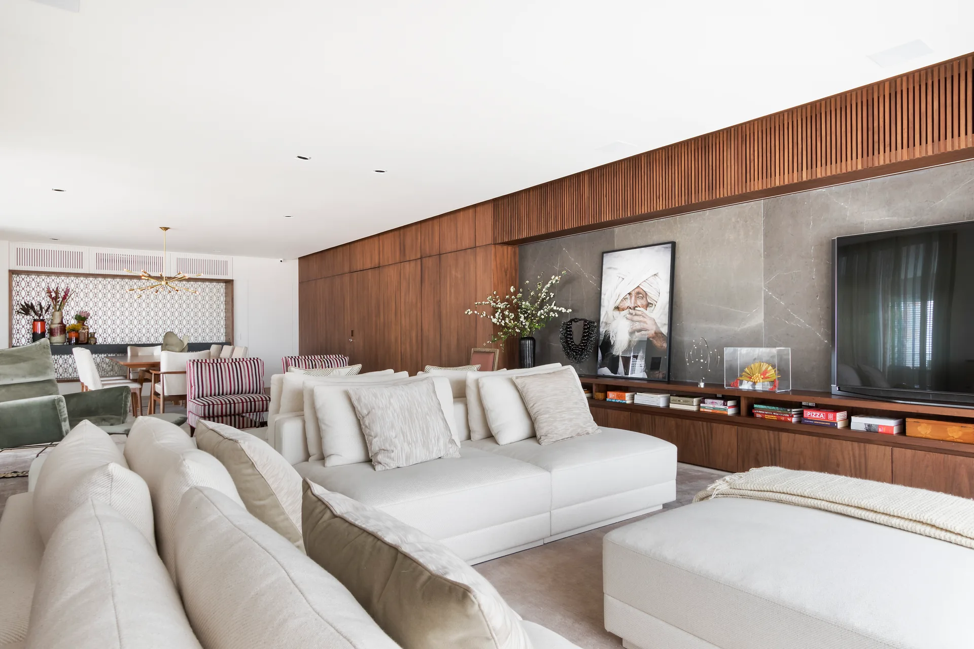 Living integrado com painel de madeira, sofá claro e sala de jantar ao fundo