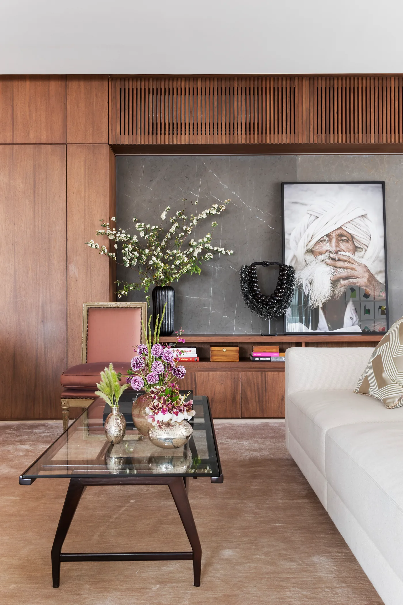 Detalhe do living com mesa de centro, flores, painel de madeira e obra de arte