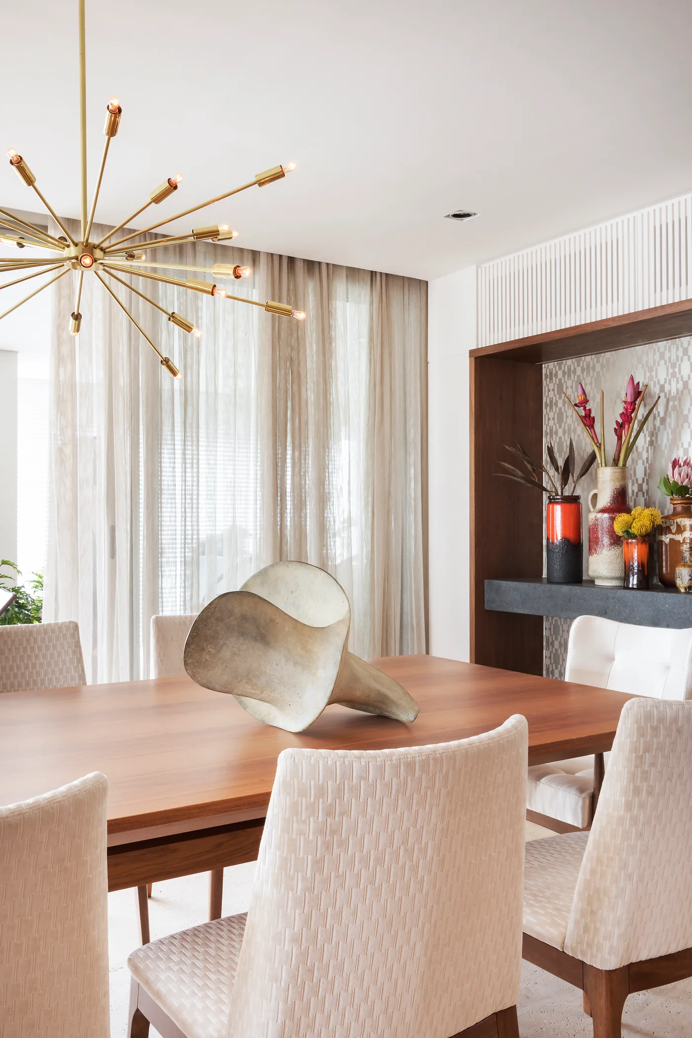 Detalhe da sala de jantar com luminária, mesa de madeira e composição floral