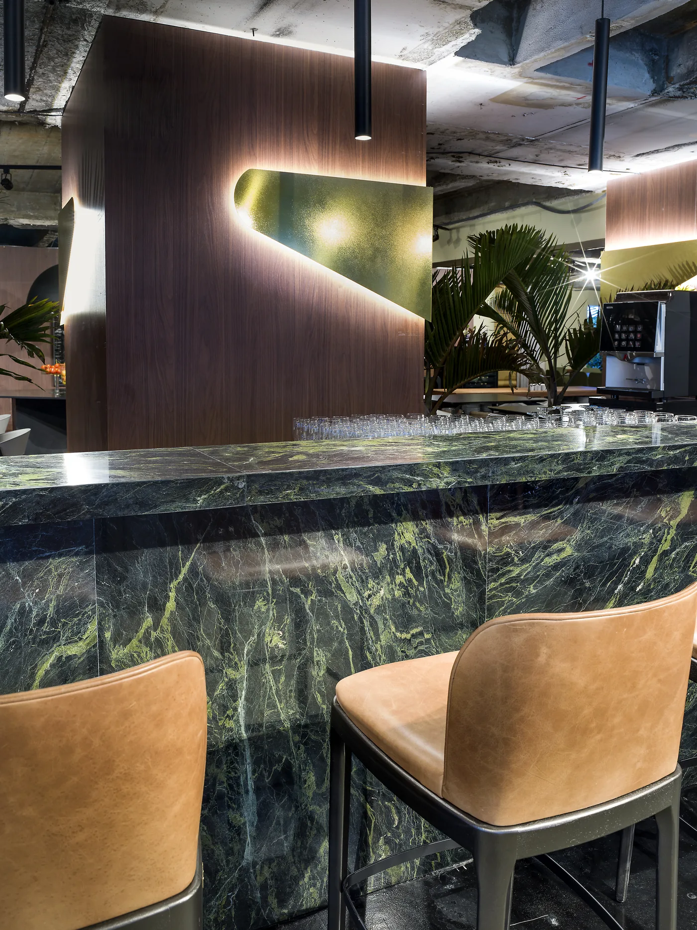 Vista próxima do bar com banquetas de couro, mármore verde e luz indireta