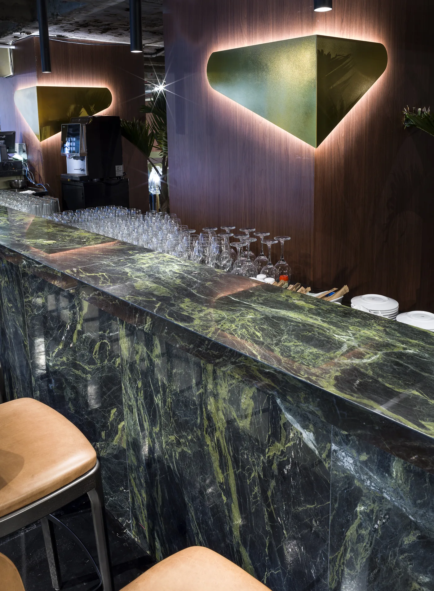 Detalhe do mármore verde do bar com cadeiras de couro e iluminação pontual