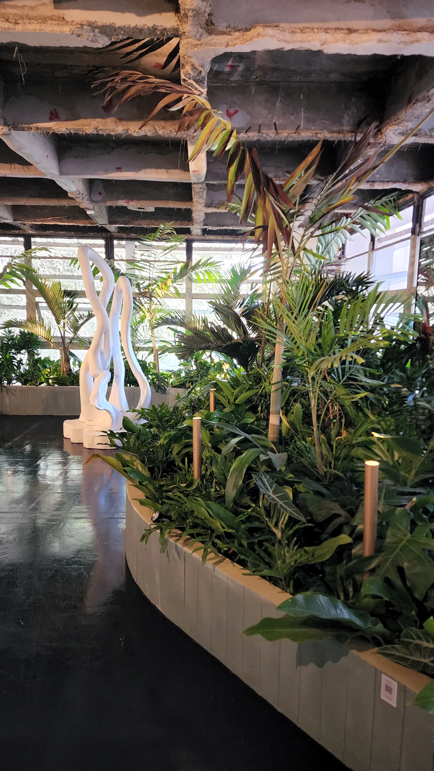 Escultura branca vista entre plantas tropicais e estrutura de concreto aparente
