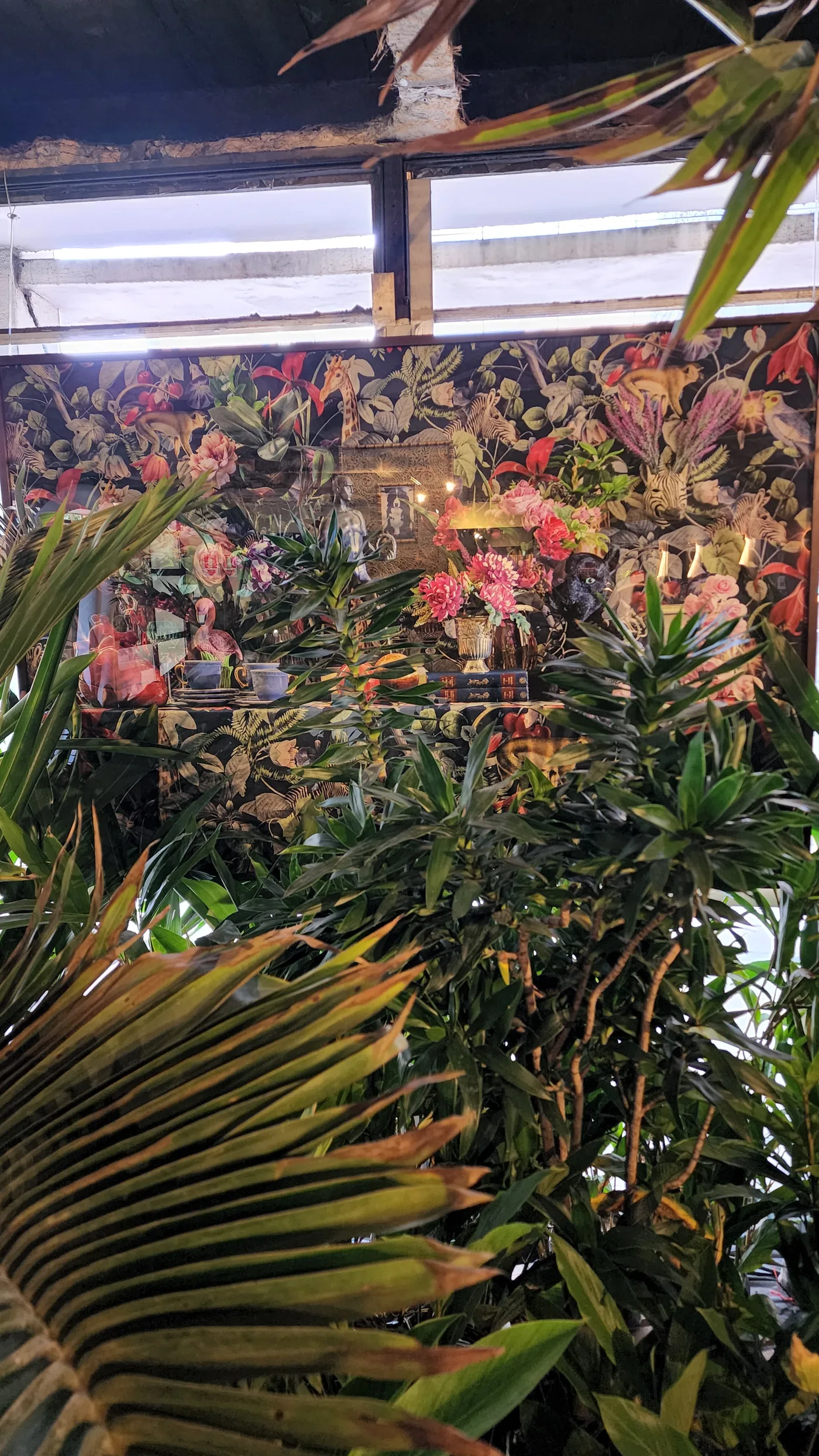 Painel com estampa tropical entre folhagens e luz natural no Restaurante Tropical