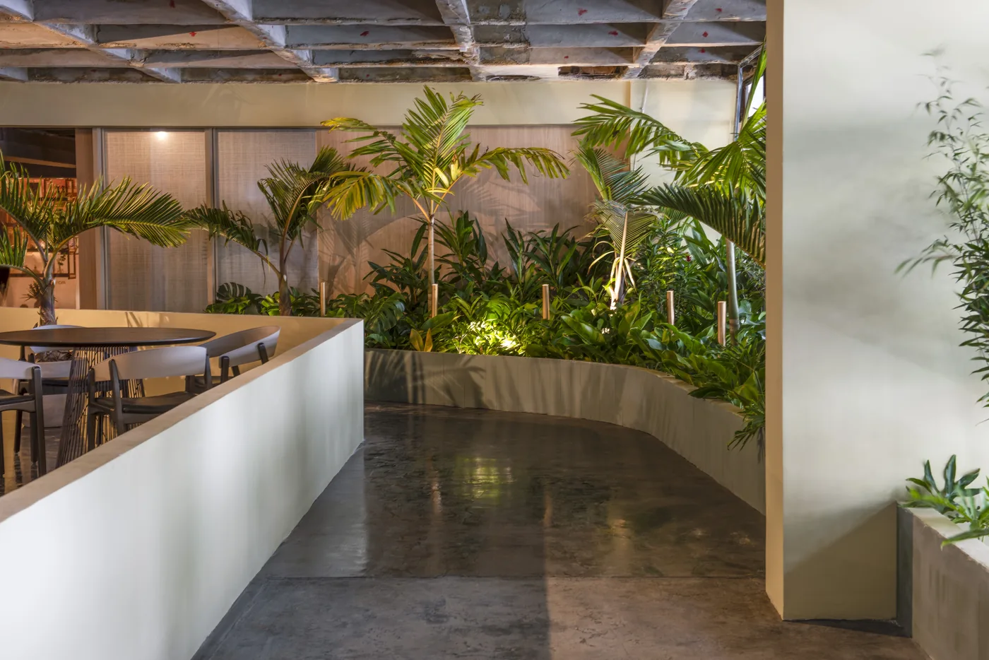 Percurso curvo do Restaurante Tropical com vegetação densa, piso escuro e mesas ao fundo