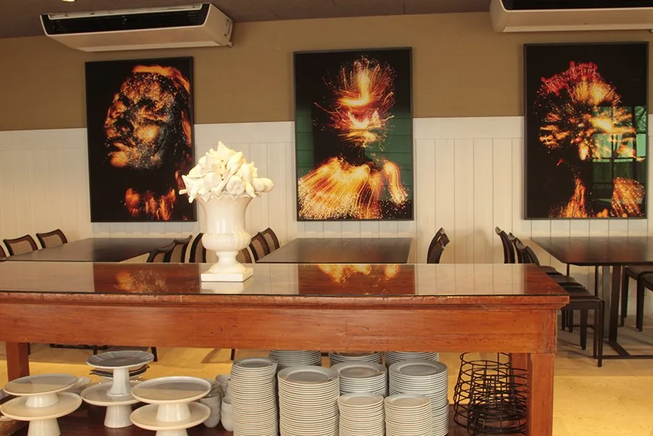 Detalhe do buffet de madeira com pilhas de pratos e três obras de arte iluminadas