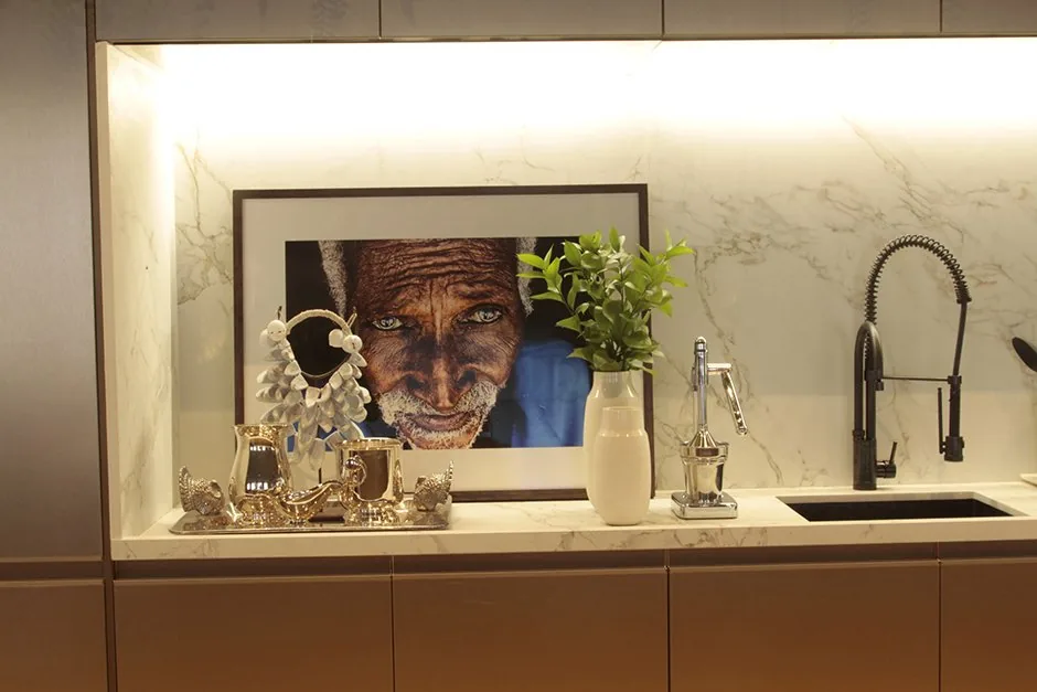 Detalhe da bancada da cozinha com mármore claro, torneira preta, vasos e fotografia