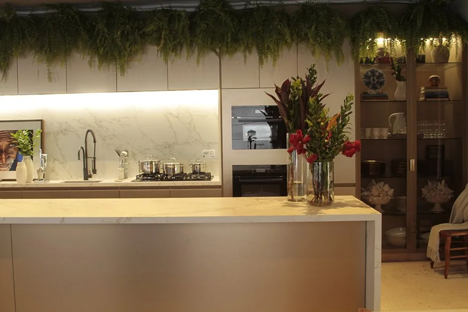 Cozinha com ilha clara, arranjo floral, armários e vegetação suspensa no ambiente BADEBEC