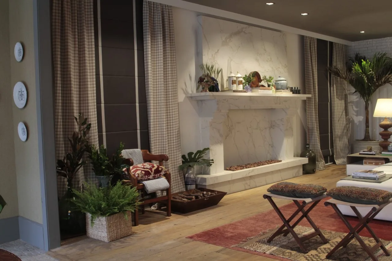 Lareira clara com plantas, cortinas xadrez e poltronas no living do restaurante