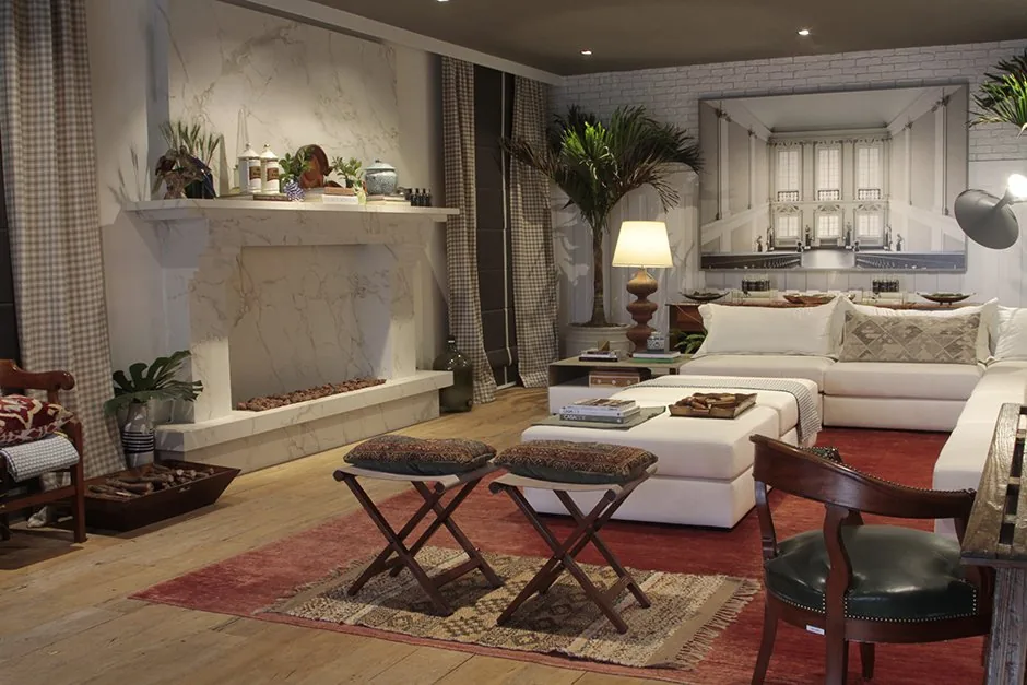 Living com lareira clara, sofá branco, tapete vermelho e mesa de centro estofada