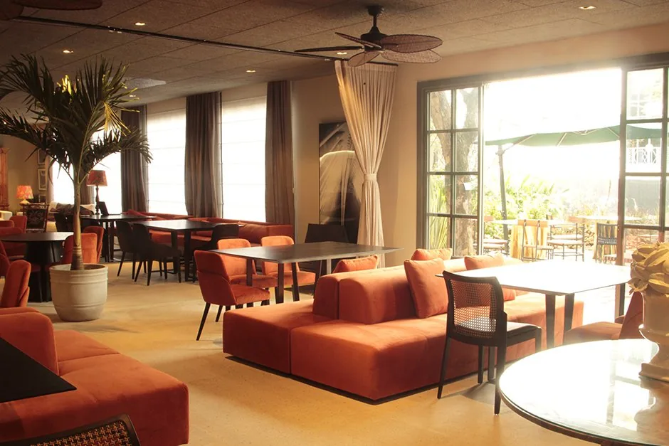 Área de estar do restaurante com sofás laranja, mesas de jantar e abertura para o jardim
