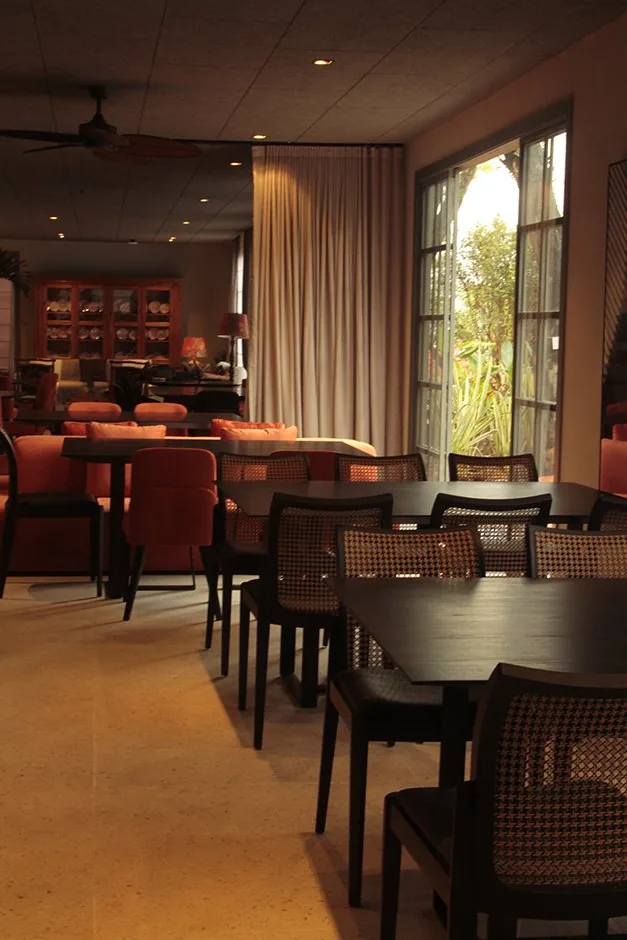 Mesas do restaurante junto à janela com cadeiras de palhinha e luz natural