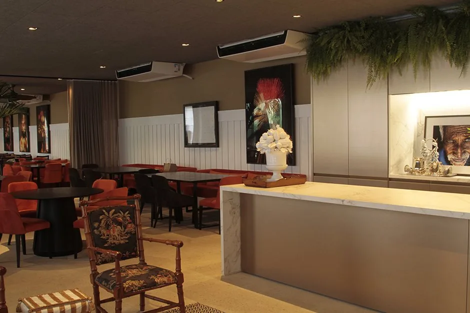 Área de recepção e bar do BADEBEC com balcão claro, plantas suspensas e poltronas