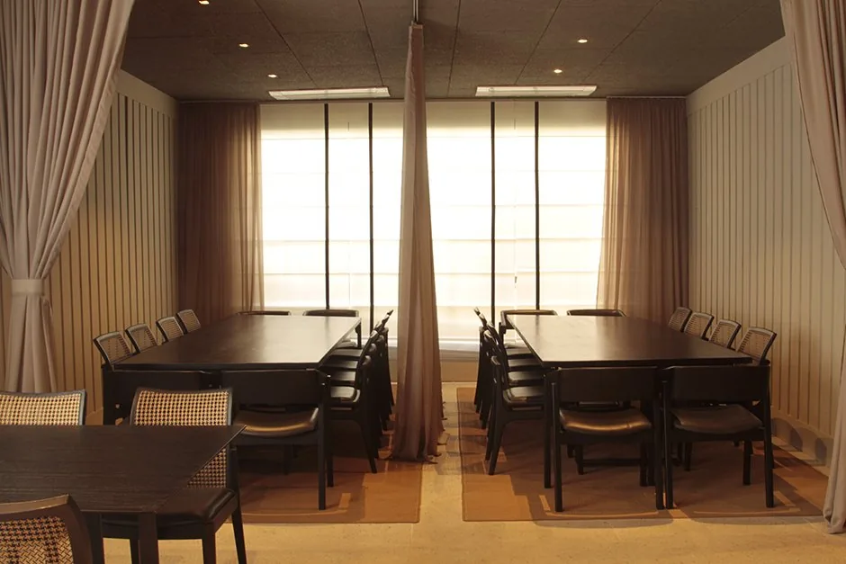 Mesas reservadas do restaurante com cortinas claras, cadeiras de palhinha e iluminação acolhedora