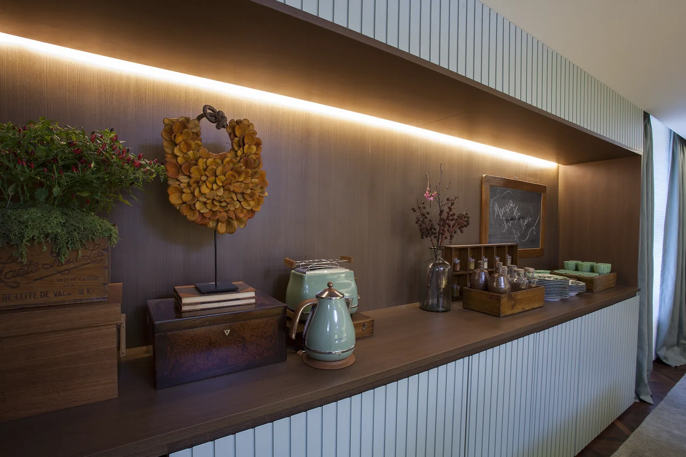 Detalhe do aparador com cafeteira, livros, flores secas e iluminação linear
