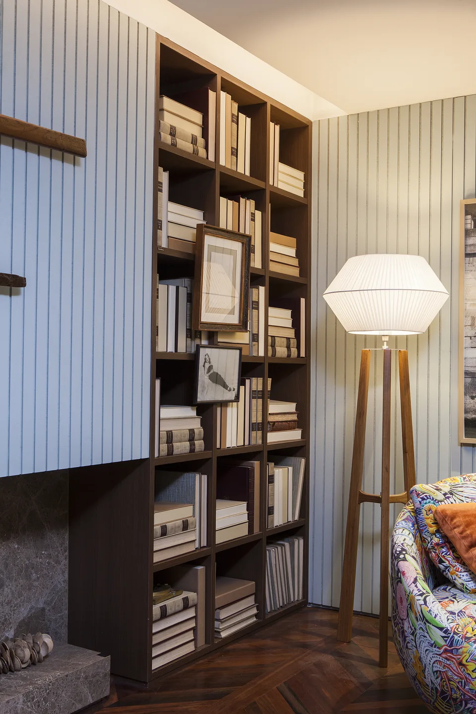 Estante com livros e luminária de piso junto à poltrona estampada