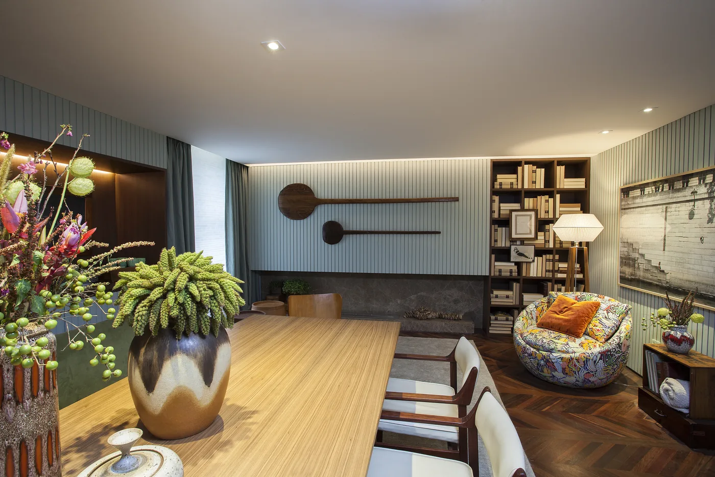 Detalhe da mesa de madeira com arranjos, louças e vista para a poltrona estampada