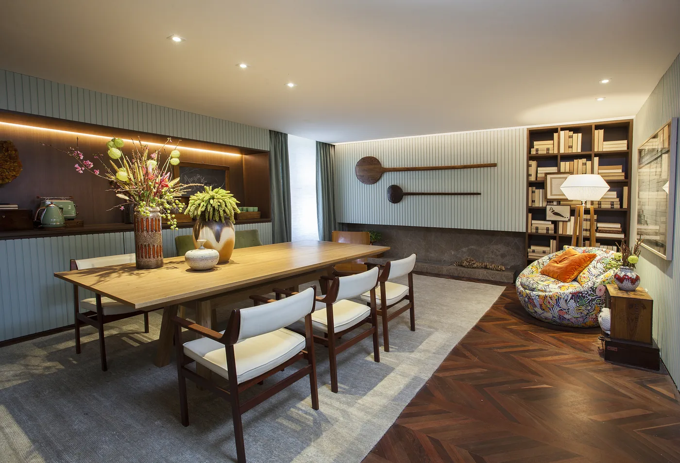 Vista ampla da Sala de Almoço CASACOR com mesa de madeira, banco verde e poltrona estampada