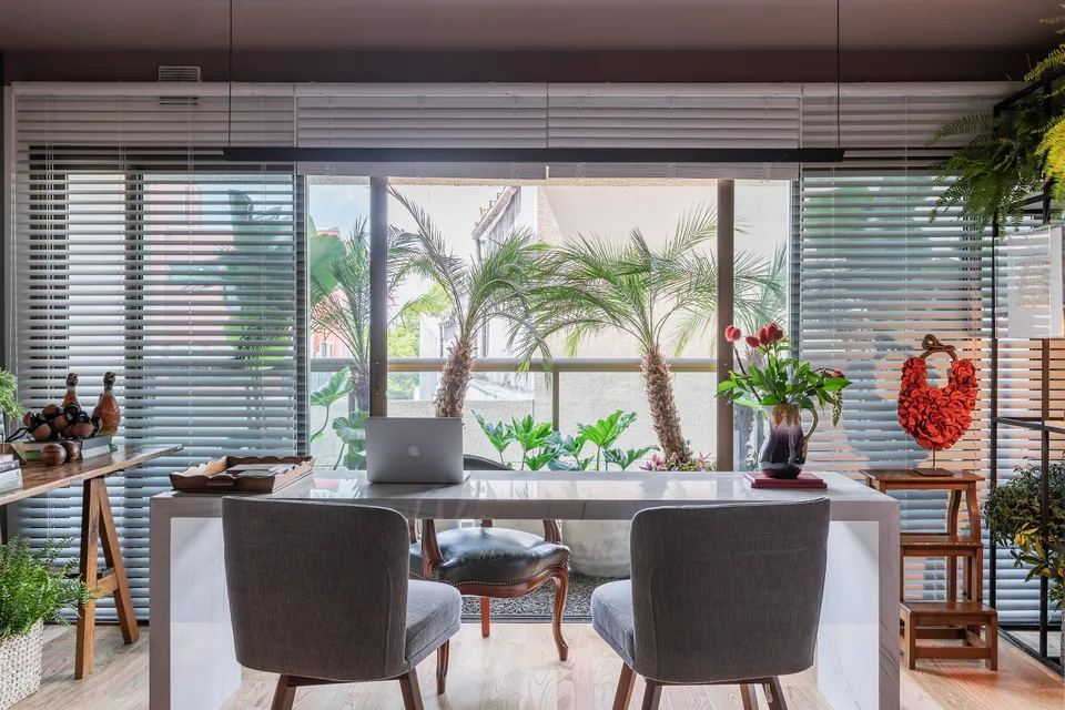 Detalhe da mesa de mármore com computador, persianas e objetos de apoio