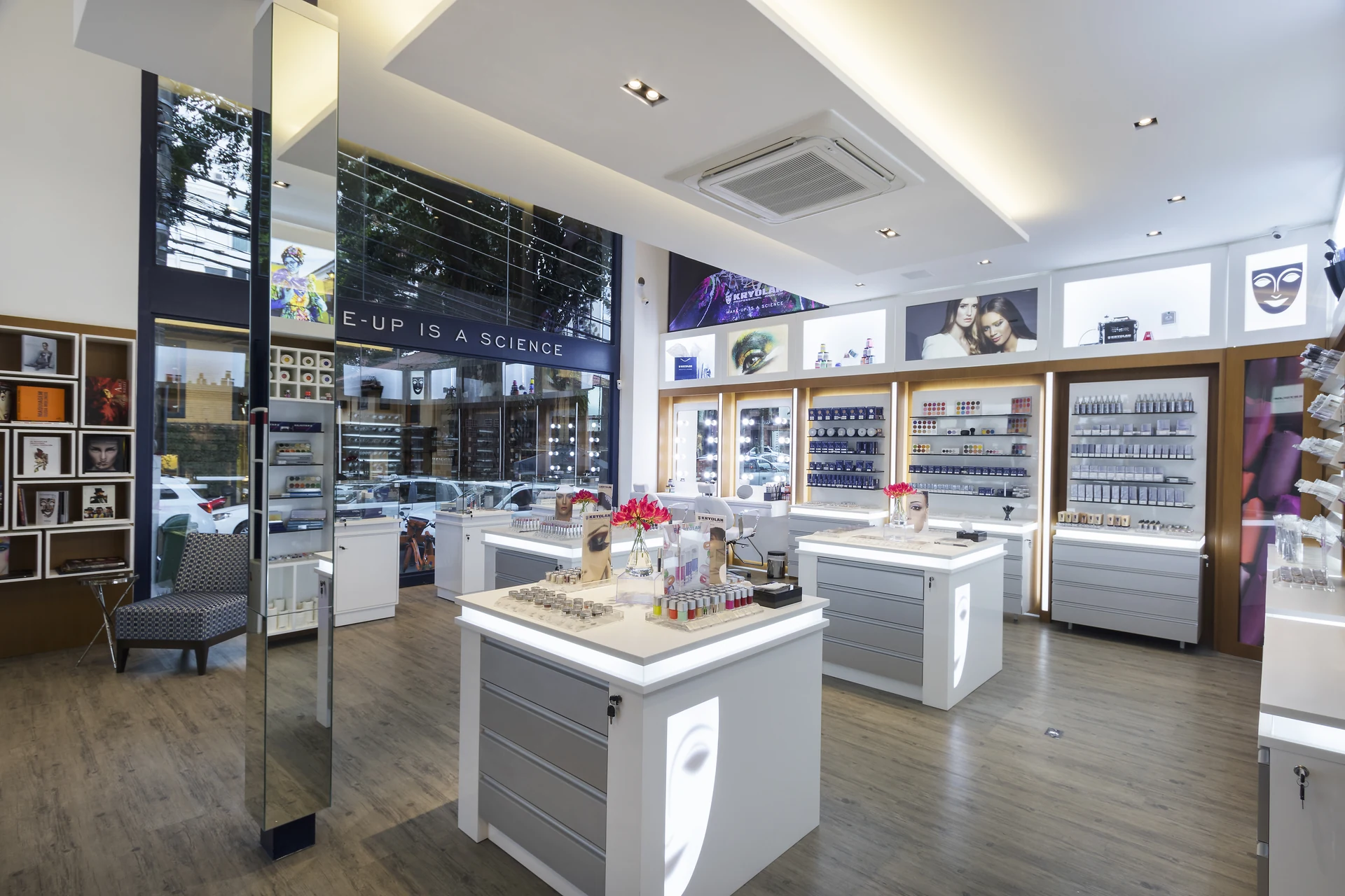 Vista ampla da Kryolan Flagship com vitrines altas, ilhas centrais e estações de maquiagem.