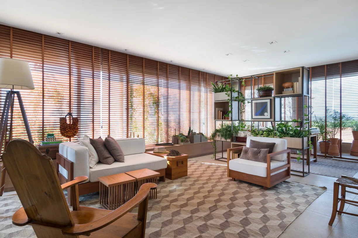 Estar da Residência Campinas - SPA com sofá, poltronas, persianas de madeira e vegetação