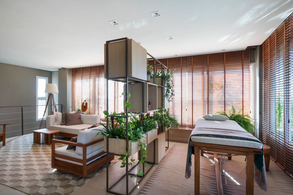 Spa com maca de massagem, estante verde, poltronas e persianas de madeira