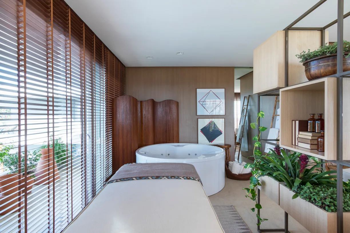 Ambiente integrado do spa com estar, maca, estante verde e banheira ao fundo